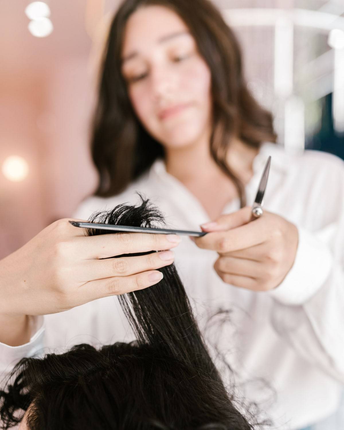 Une coiffeuse tient une mèche entre son peigne et ses ciseaux, au-dessus de la tête d'une cliente.