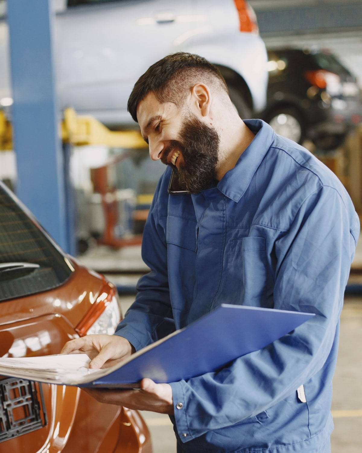 Un mécanicien souriant consulte un dossier près d'une voiture, dans son garage.