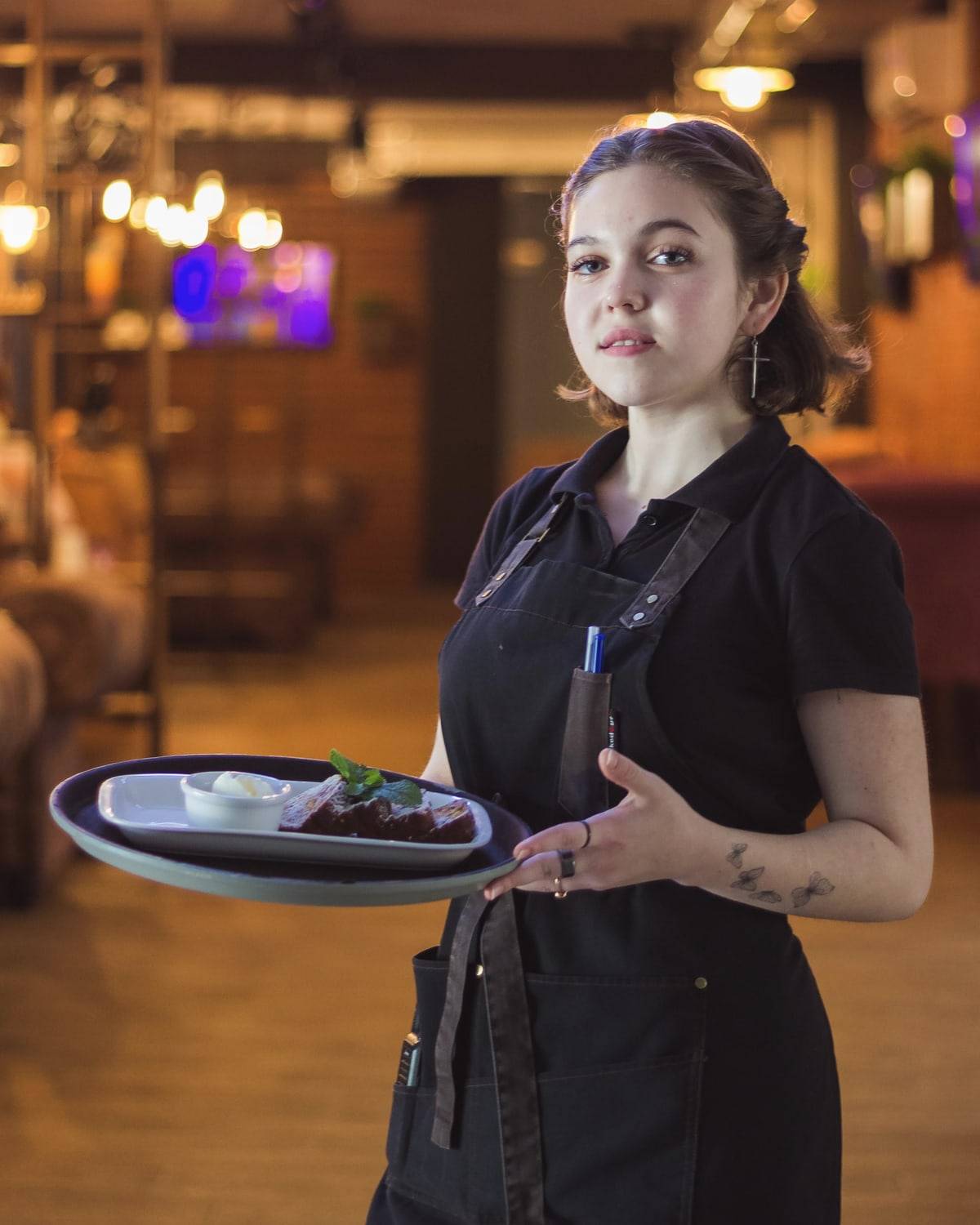 Une serveuse souriante tient une assiette de dessert dans la salle d'un restaurant.